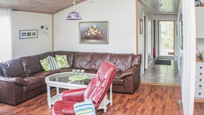 Una sala de estar con un sofá de cuero marrón, una mesa de centro de vidrio, una silla roja y un cuadro en la pared.