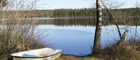 Un petit bateau est amarré à un arbre au bord d’un lac paisible, lui-même entouré d’arbres.