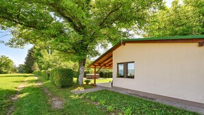 Uma casa moderna com varanda coberta, gramado bem cuidado e uma grande árvore que oferece sombra.