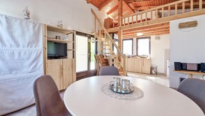 Um quarto aconchegante e bem iluminado, com escada de madeira, mesa de jantar com cadeiras, televisão e área de cozinha.