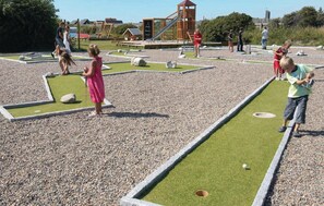 A children's play area with a mini-golf setup, a wooden play structure, and a small building in the background. - Stunning home in Thyborøn with WiFi (Thyborøn)