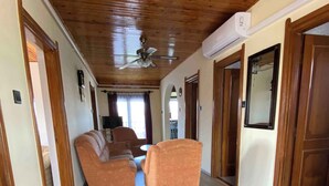 Un corridoio con pavimento e pareti in legno, che conduce a un soggiorno con due poltrone arancioni e un divano.