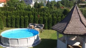 Una piscina all'aperto circondata da un prato curato, un gazebo e un siepe.