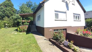 A two-story house with a sloped roof, satellite dish, and a small porch with potted plants. - Holiday home in a quiet location with terrace (Agárd)