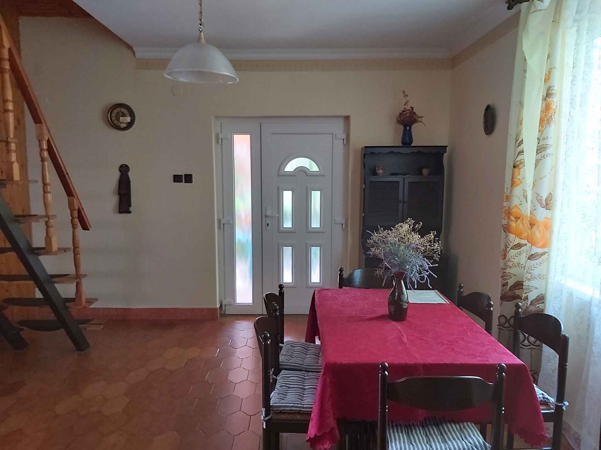 A dining area with a red tablecloth, a vase with flowers, and a staircase leading to a door.