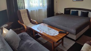 A hotel room with a bed, a sofa, a wooden table with a lace tablecloth, a chair, a nightstand, a lamp, and a painting on the wall. - Holiday home in a quiet location with terrace (Agárd)
