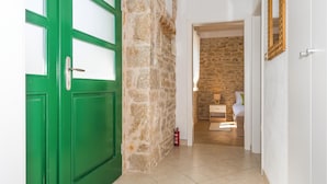 A hallway with a green door, stone wall, and a bedroom with a bed, nightstand, and a lamp.
