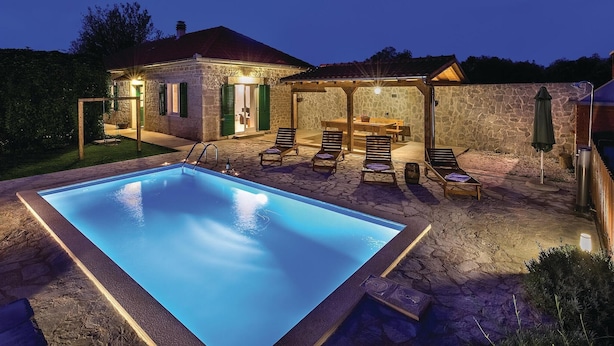 A stone pool with lounge chairs and a covered seating area at dusk.