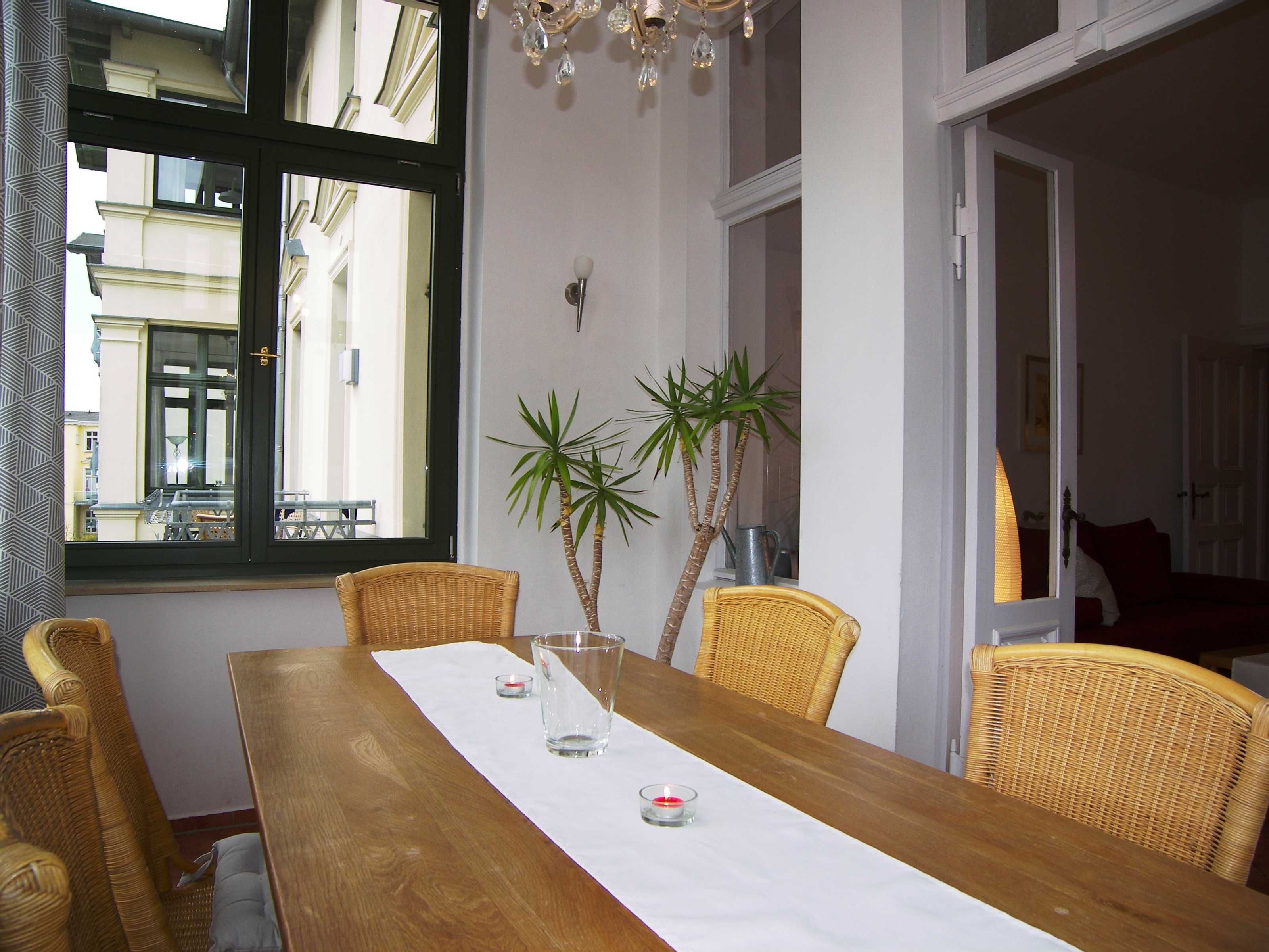 Ein Essbereich mit Holztisch, Korbstühlen, zwei Zimmerpflanzen und einer Chandelier.