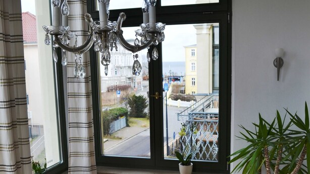 A room with a large window, a chandelier, a wicker chair, and a potted plant.