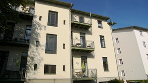 A multi-story residential building with balconies, windows, and a car parked in front.