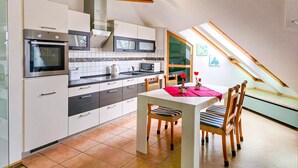 A modern kitchen with built-in appliances, a dining area with a table and chairs, and a sloped ceiling with skylights.