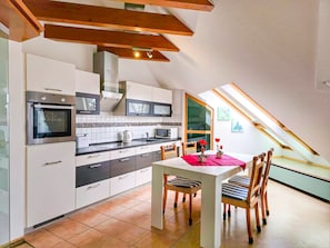 A modern kitchen with built-in appliances, a dining area with a table and chairs, and a sloped ceiling with skylights.