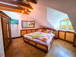 A bedroom with a wooden bed, a large window, a mirror, and a television on the wall.