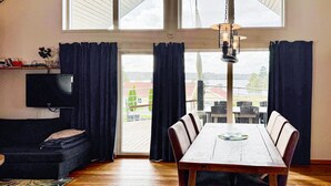 A dining area with a wooden table and chairs, a black sofa, a flat-screen TV, and a view of a building and trees through large windows. - 1 bedroom amazing home in Månsarp (Månsarp)