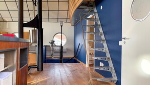 A room with a wooden floor, a metal ladder, a window, and a door with a circular design. - 1 bedroom amazing home in Månsarp (Månsarp)