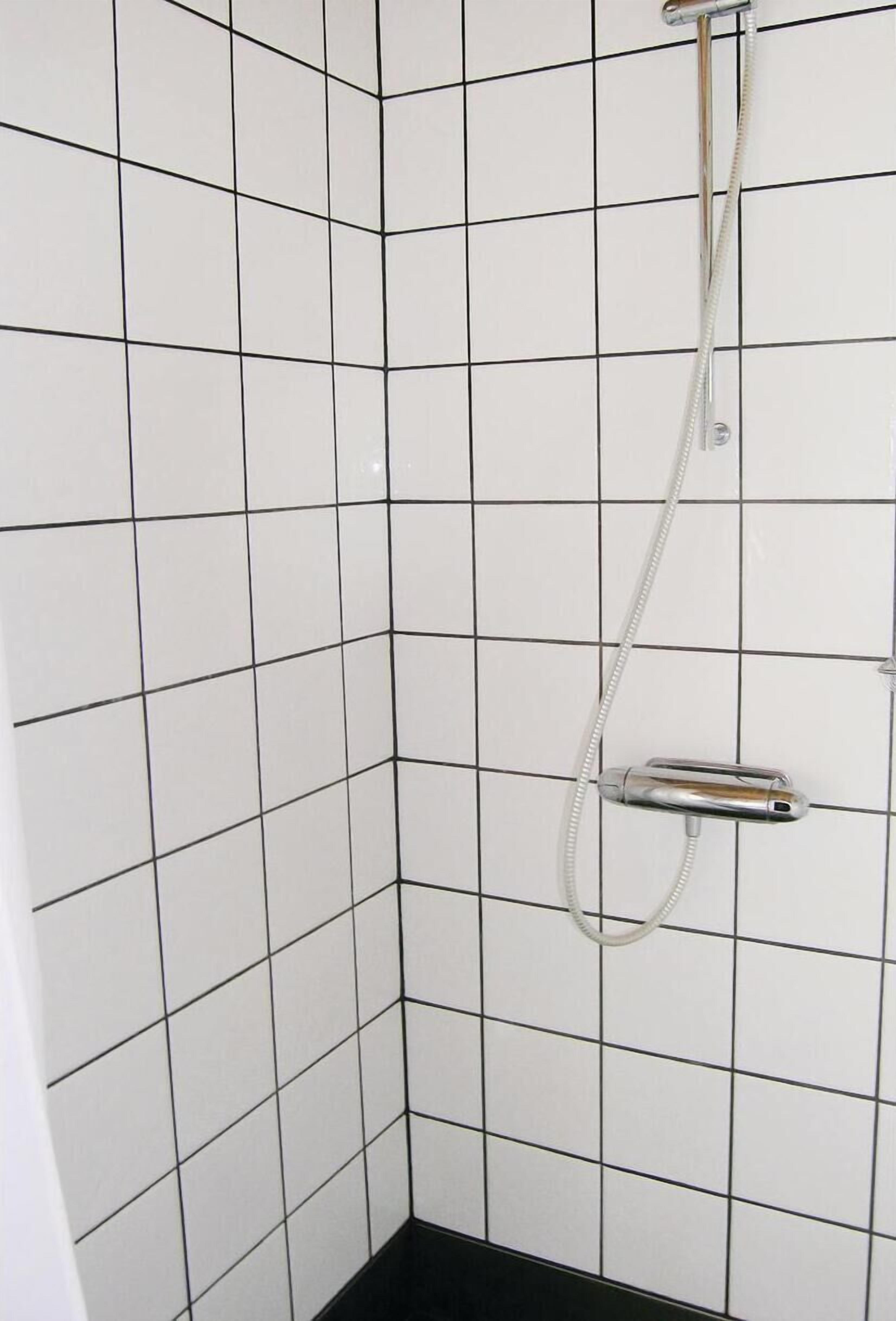 A tiled shower area with a handheld showerhead and a wall-mounted control.