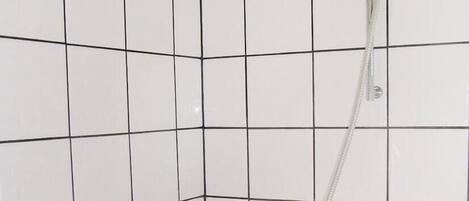 A tiled shower area with a handheld showerhead and a wall-mounted control.