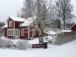 Une maison rouge à deux étages, dont le toit et la cour sont recouverts de neige.