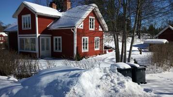 Une maison rouge, avec un toit recouvert de neige et un grand tas de neige devant.
