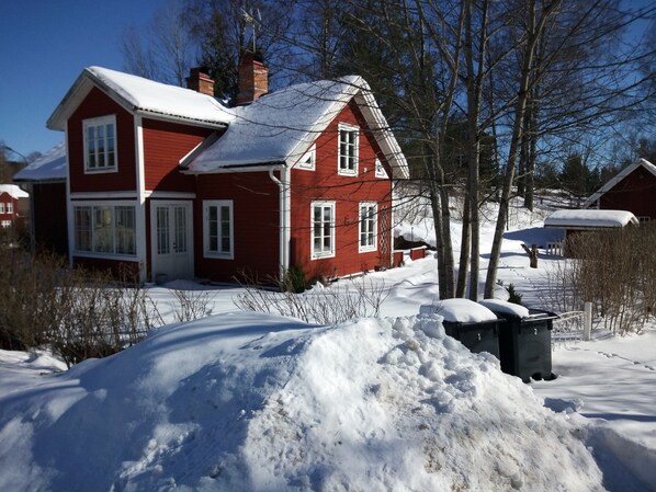 A red house with a snow-covered roof and a large pile of snow in front.