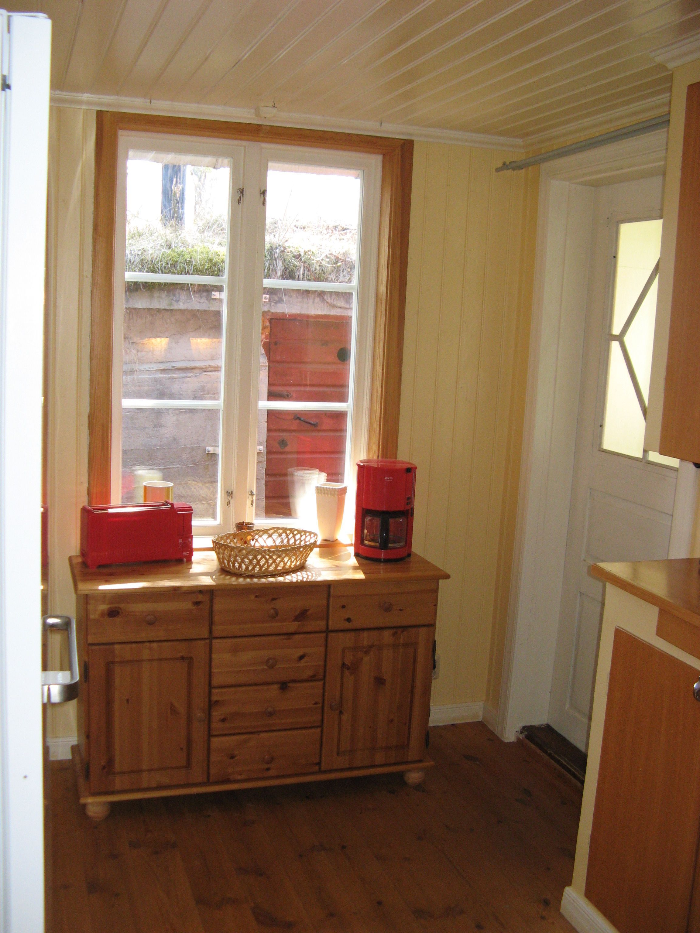 A kitchen with wooden cabinets, a window, and a red coffee maker.