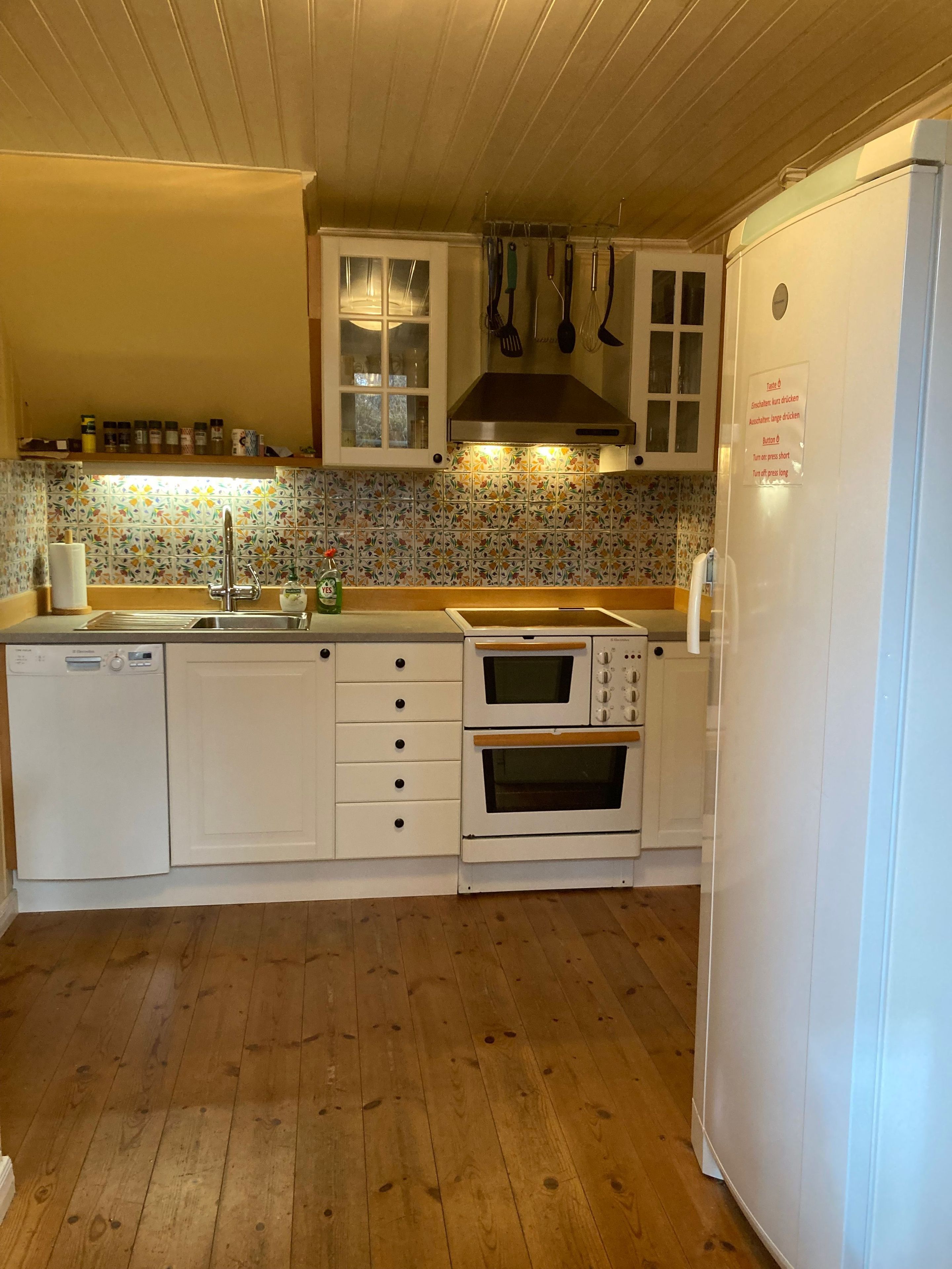 Une cuisine avec des meubles de rangement en bois, un four encastré, un lave-vaisselle et un réfrigérateur.