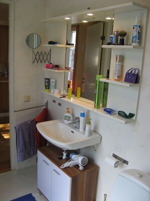 A bathroom with a sink, mirror, shelves with toiletries, and a towel rack.