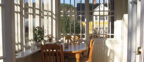 Une pièce avec une table et des chaises en bois, de grandes fenêtres et une vue sur les bâtiments environnants.