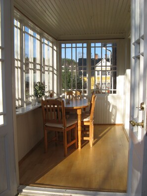 A room with a wooden table and chairs, large windows, and a view of buildings outside.