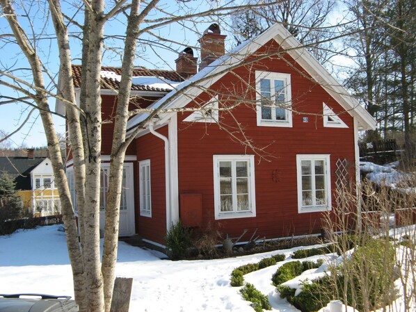 Una casa roja con detalles blancos, una chimenea y un patio cubierto de nieve.