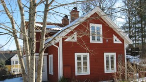 Et rødt hus med hvide detaljer, skorsten og en gård dækket af sne.
