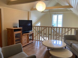 Una sala de estar acogedora con un televisor sobre un mueble de madera, una mesa redonda y dos sillones.