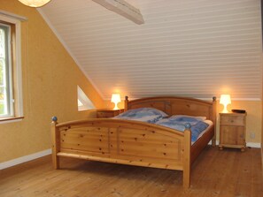 A bedroom with a wooden bed, two bedside tables with lamps, a window, and a sloped ceiling.