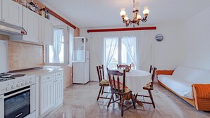 Une cuisine avec des meubles blancs, un fourneau et un coin repas comprenant une table ronde et des chaises.