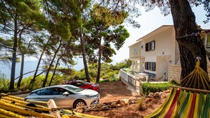 Une maison à deux étages avec un patio, un hamac et une voiture garée devant.