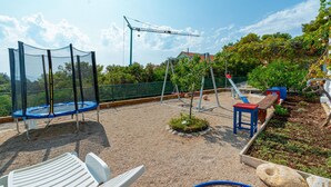 Un espace de jeux extérieur avec un trampoline, des balançoires et un toboggan.