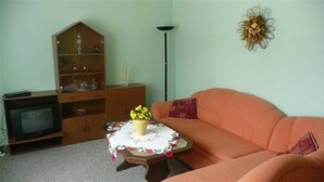 Ett vardagsrum med ett träskåp, en tv, ett blommigt bordsduk och en orange soffa.