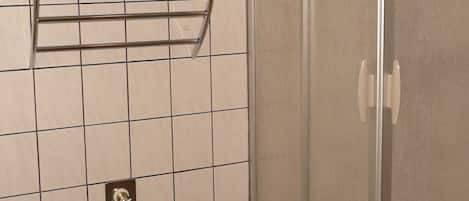 A bathroom with a shower enclosure, a towel rack, a sink, and a decorative wall piece.