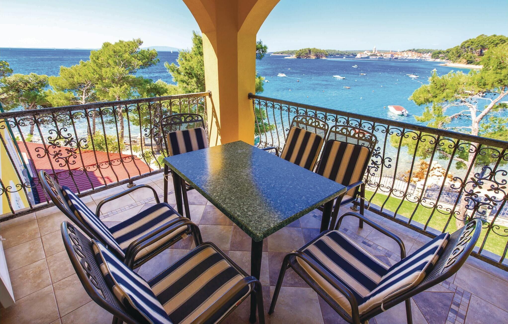 Un balcón con mesa y sillas, con vistas a una zona costera con barcos y vegetación.