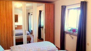 A bedroom with two beds, a wardrobe, a window with curtains, and a radiator.