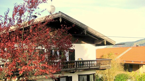 A two-story house with a balcony, a satellite dish, and a garden.