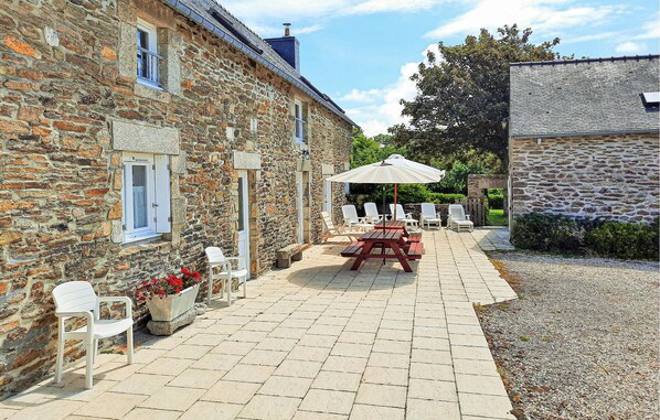 A stone building with a patio area featuring a table and chairs, a covered seating area, and a gravel path. - Beautiful home in Clohars Carnoet (Clohars Carnoet)