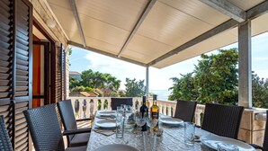 Een buiten eethoek met een tafel voor vier personen, omringd door rieten stoelen, onder een overdekt terras.
