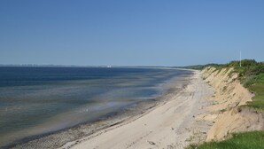 Rantaviiva, jossa on kirkas taivas, hiekkainen ranta ja ruohokasvuinen kallio.
