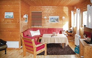Cozy cabin room with a comfortable sofa, armchair, and television, surrounded by framed pictures.
