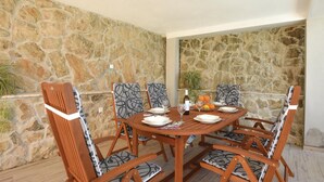 A stone-walled outdoor dining area with a round wooden table set for four, surrounded by patterned chairs.