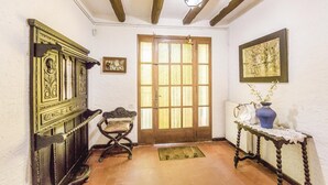 Une pièce avec une porte en bois, une chaise, une petite table sur laquelle se trouve un vase, et un tableau accroché au mur.