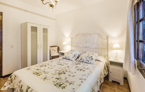A bedroom with a bed, two bedside tables, a chair, a wardrobe, and a chandelier. - Awesome home in Riudoms (Riudoms)