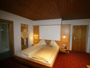 A bedroom with a wooden ceiling, a bed, a wardrobe, a mirror, and a door.